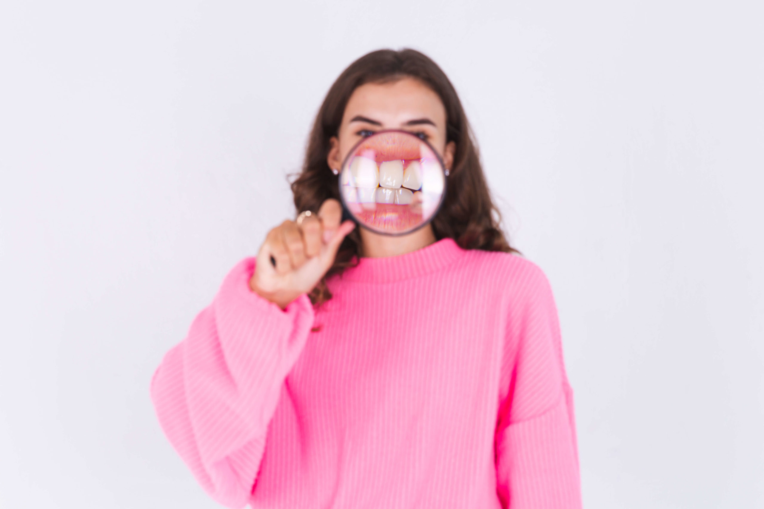 young beautiful woman with freckles light makeup sweater white wall with magnifier shows white teeth perfect smile 2 1 1 scaled - Myobrace: o tratamento que promete alinhar os dentes